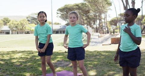 Diverse schoolgirls standing on grassy field during outdoor pe activity in mint shirts