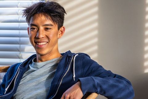 Asian teenage male smiling while sitting in sunlit living room wearing navy hoodie with earring