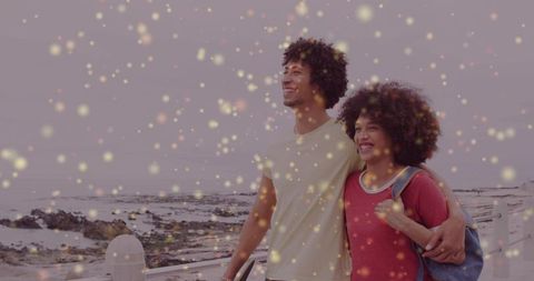 Young couple walking seaside promenade embracing with golden bokeh and joyful smiles