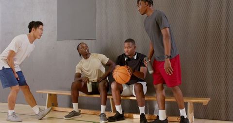 Friends playing basketball on gym bench, teammates talking and laughing