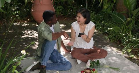 Multicultural friends enjoying relaxing picnic in lush garden outdoors