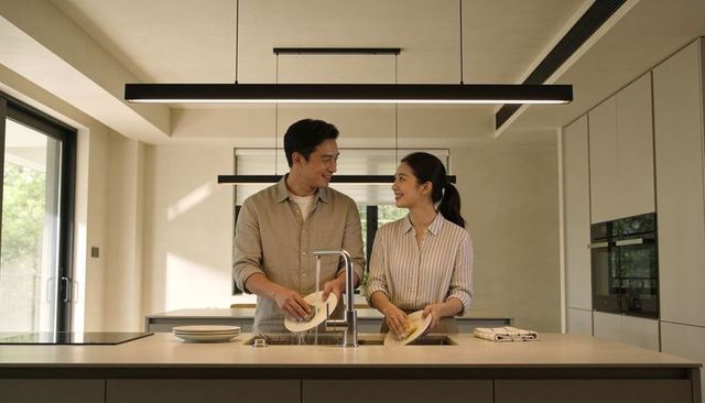 Young couple washing dishes at modern minimalist kitchen island, sharing smile