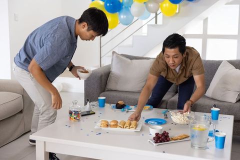 Asian friends arranging party snacks on living room coffee table with balloons