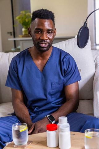 Black male medical worker recording healthcare podcast on sofa with medication bottles