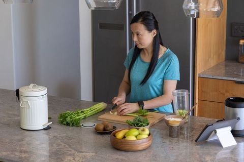 Asian woman chopping celery on wooden cutting board at modern kitchen island with tablet