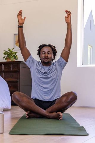 African man meditating at home on green mat with arms raised morning yoga calm peaceful