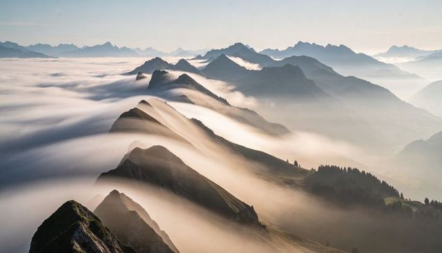 Serrated mountain ridge slicing through low clouds and mist at dawn with sunlit crests