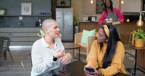 Two women chatting over coffee in modern cafe, casual conversation, smartphone in hand