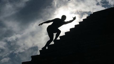 Silhouette Male Athlete Climbing Ancient Ruin Steps Backlit by Dramatic Cloudy Sky