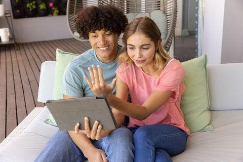 Young couple sharing video call on tablet while relaxing on patio sofa