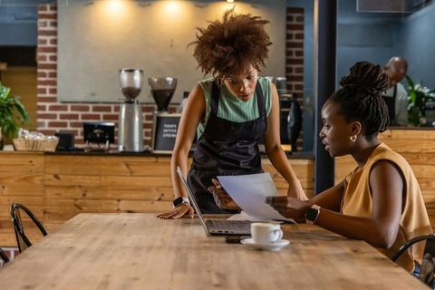 Barista and customer reviewing documents at rustic coffee shop laptop collaboration