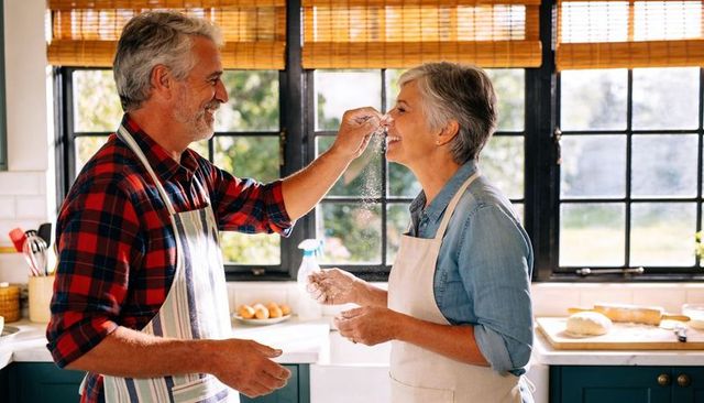 Senior couple playfully sprinkling flour while baking together in sunlit home kitchen