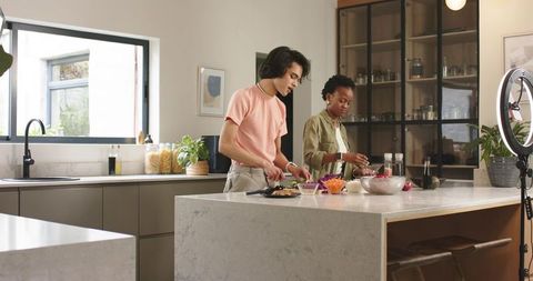 Diverse couple preparing healthy meal on marble island while filming cooking vlog