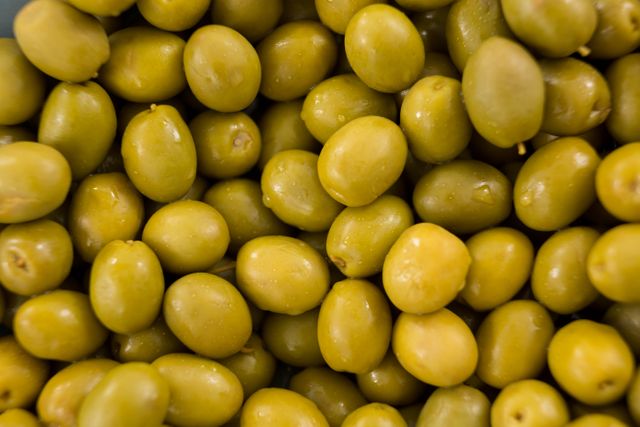 Close-up of marinated green olives, showcasing their texture and vibrant color. Ideal for use in food blogs, recipe websites, culinary magazines, and health and nutrition articles. Perfect for promoting Mediterranean cuisine, healthy eating, and gourmet appetizers.