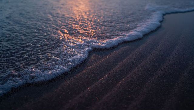 Sunset Glow Washing Over Dark Sand Shoreline with Foamy Wave and Sparkling Ripples