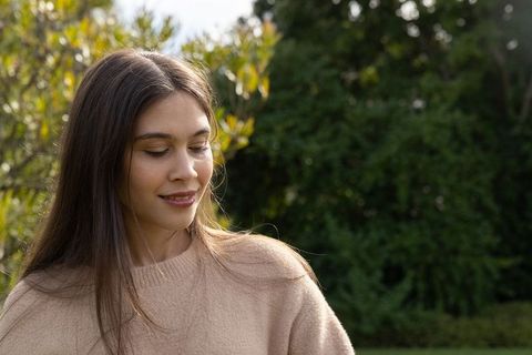 Serene young woman standing in garden wearing beige sweater enjoying soft natural light