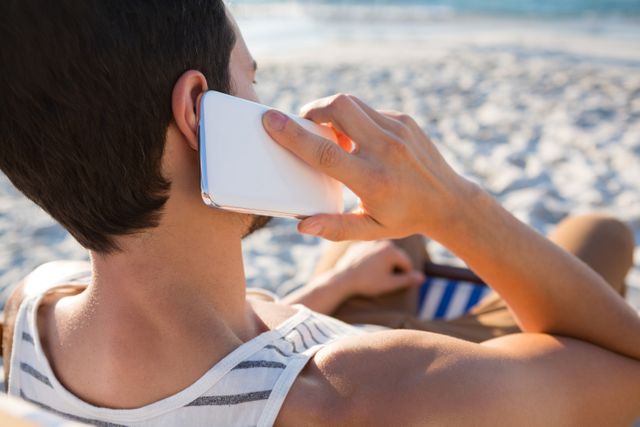 Man talking on mobile phone while relaxing at beach during sunny day