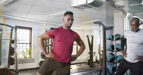 Pausing man with hands on hips during strength training with medicine ball rack and coach