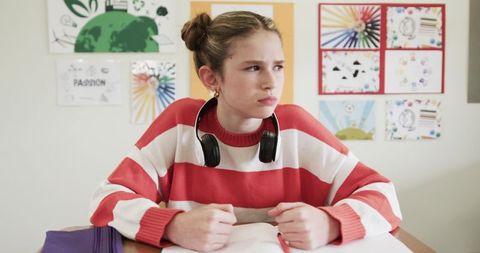 Focused Teen Girl Writing in Classroom with Headphones
