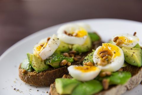 Avocado toast topping with soft-boiled eggs and toasted pine nuts on whole grain bread