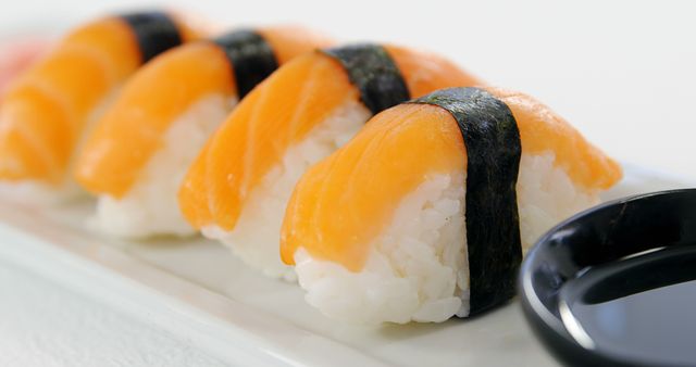 A row of salmon nigiri sushi is elegantly presented on a white plate, accompanied by a small dish of soy sauce. Sushi, a traditional Japanese dish, is enjoyed worldwide for its fresh flavors and artistic presentation.