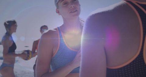 Sunlit women beach volleyball team communicating during match with lens flare