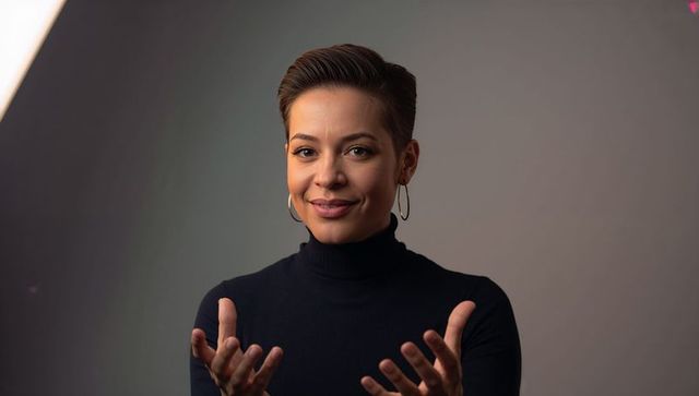 Confident woman presenting and gesturing, black turtleneck and hoop earrings, studio portrait