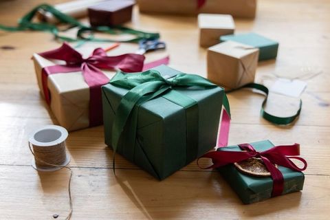 Green satin-wrapped gift sitting on wooden table with kraft-wrapped presents and twine