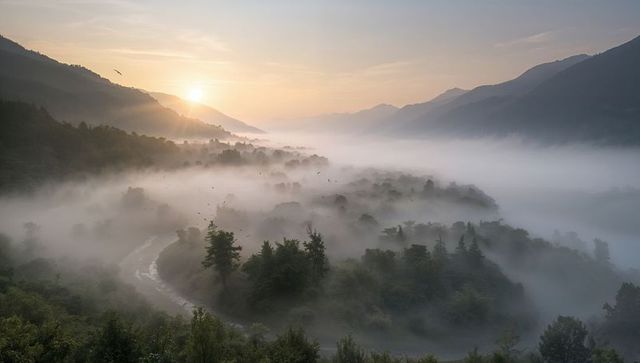 Rising sun illuminating misty mountain valley with meandering river and birds