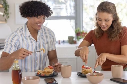 Young diverse couple enjoying pancake breakfast together in bright cozy home kitchen morning light
