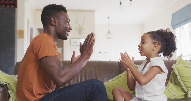 African american daughter and father having fun playing clapping game together in living room. Fatherhood, childhood, fun, togetherness and domestic life.