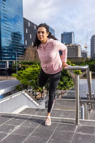 Active woman stretching on urban stairs using handrail before outdoor workout in city