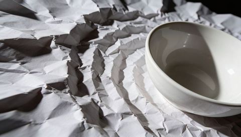 White porcelain bowl reflecting light on crumpled paper with dramatic high-contrast shadows