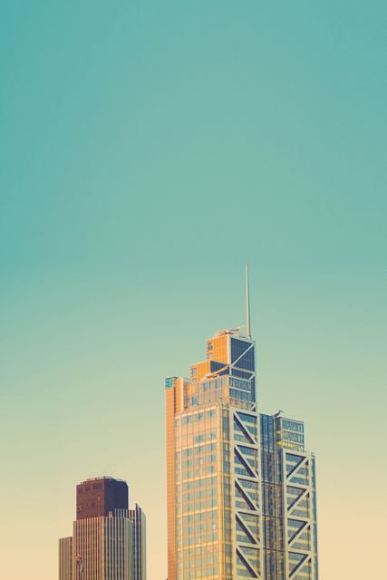 Urban skyscrapers seen against a soft pastel sky during sunset. The image captures two prominent tall buildings in a modern city environment. This stock photo can be used for themes related to urban growth, architectural design, business districts, and modern city living.