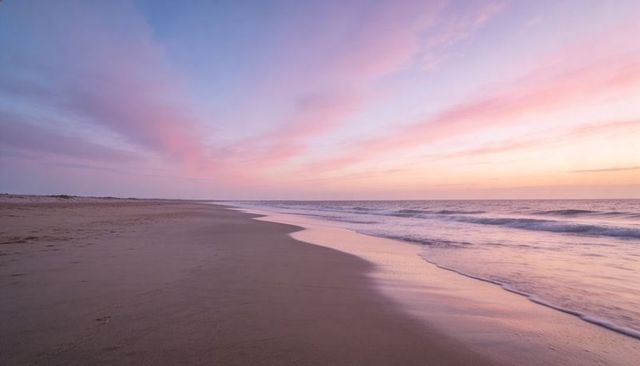 Pastel sunrise over empty beach with reflective wet sand and gentle ocean waves