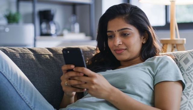 Young woman reclining on couch scrolling smartphone, relaxed home lifestyle moment
