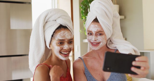 Diverse happy female friends wearing towels on heads and cleansing masks taking selfie at home. female friends hanging out enjoying leisure time together.