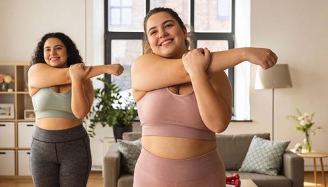 Curvy women stretching together during home workout with dumbbells and positive energy