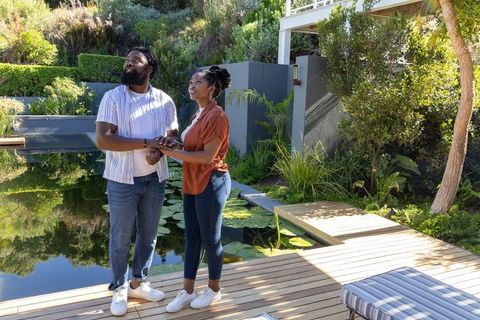 African american couple holding hands looking up on modern backyard deck in garden beside pond