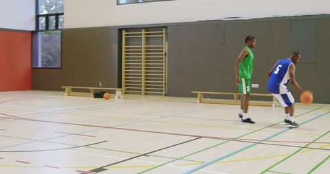 African american guard dribbling crossover as defender pressing on indoor court