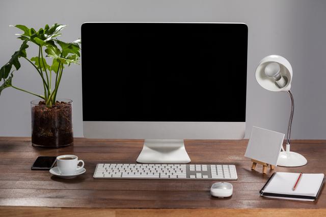 Modern office desk featuring a computer, keyboard, mouse, desk lamp, plant, coffee cup, notebook, and smartphone. Ideal for illustrating professional work environments, productivity, and office setups. Suitable for business, technology, and organizational themes.