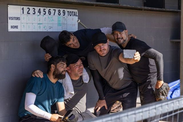 Baseball dugout selfie with diverse adult teammates posing, laughing, showing camaraderie