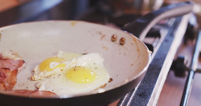 Image of eggs and bacon frying in a skillet on a gas stove. Perfect for use in cooking blogs, food recipes, breakfast ideas, or culinary websites. The sizzling sounds and aroma are implied, adding warmth and a sense of home cooking.