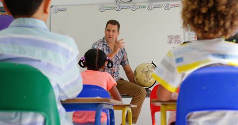Male teacher engaging diverse students with globe in classroom setting