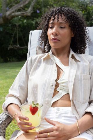African american woman lounging in garden holding lemonade glass topped with strawberry