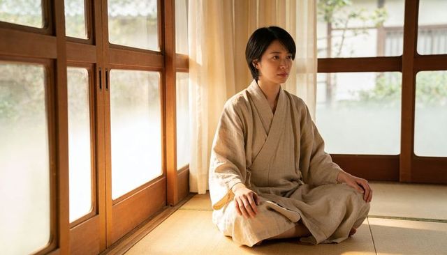 Asian woman sitting in kimono on tatami meditating by wooden sliding doors in minimalist room