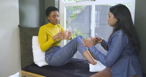 Diverse female friends sharing drinks on cozy window seat