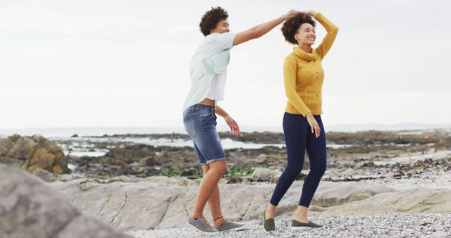 Couple is dancing on a rocky beach with happy expressions. They are casually dressed and appear to be enjoying the moment. Ideal for use in lifestyle magazines, dating and relationship blogs, and travel brochures.