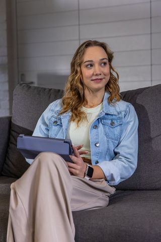 Young woman using tablet on sofa wearing denim jacket and smartwatch in modern living room