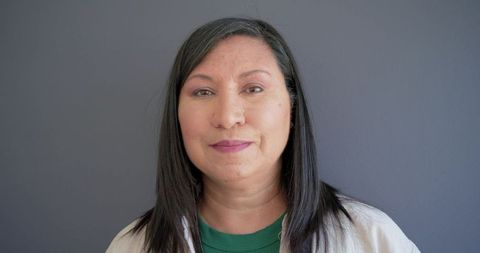 Mature woman posing for corporate headshot with neutral gray backdrop, confident approachable
